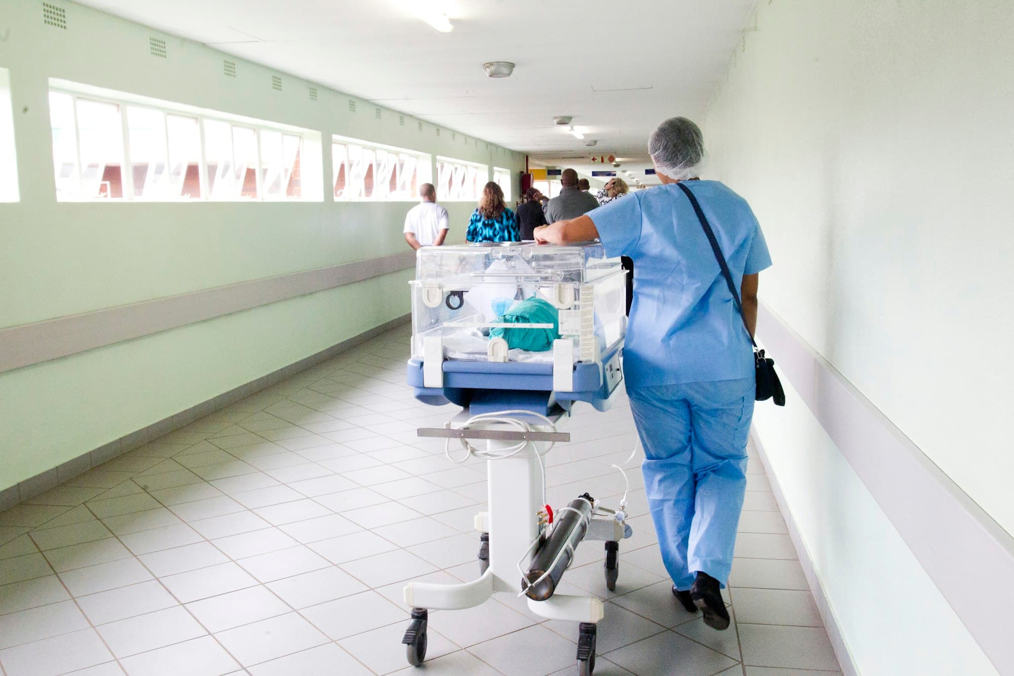 A nurse wheeling a humidicrib down a bright hospital corridor
